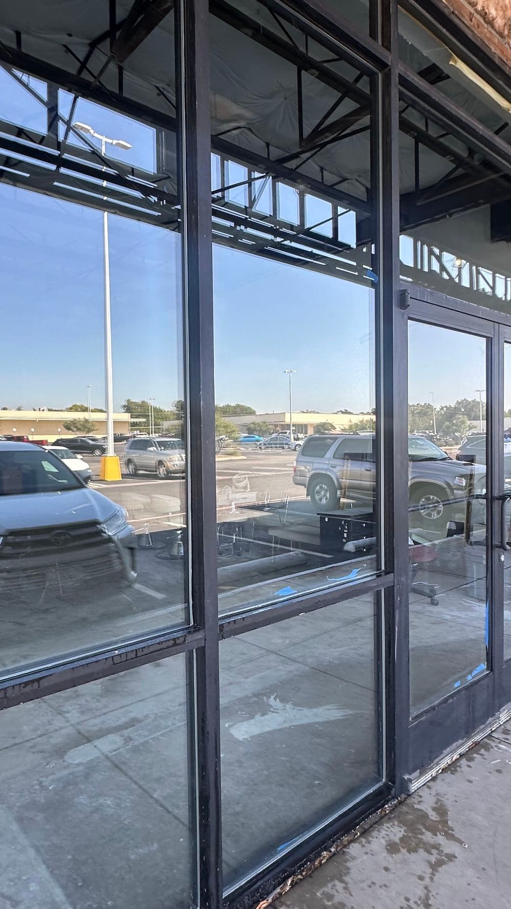 Exterior view of a glass storefront reflecting parked cars and a blue sky.