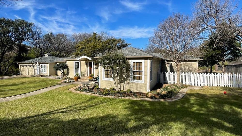 Charming single-story house with landscaped yard and white picket fence under clear blue sky.