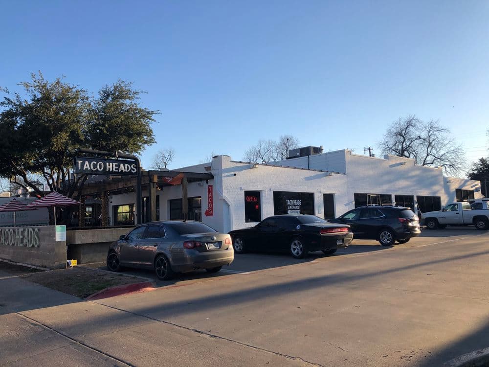 Taco Heads restaurant exterior with parked cars and clear blue sky in background.