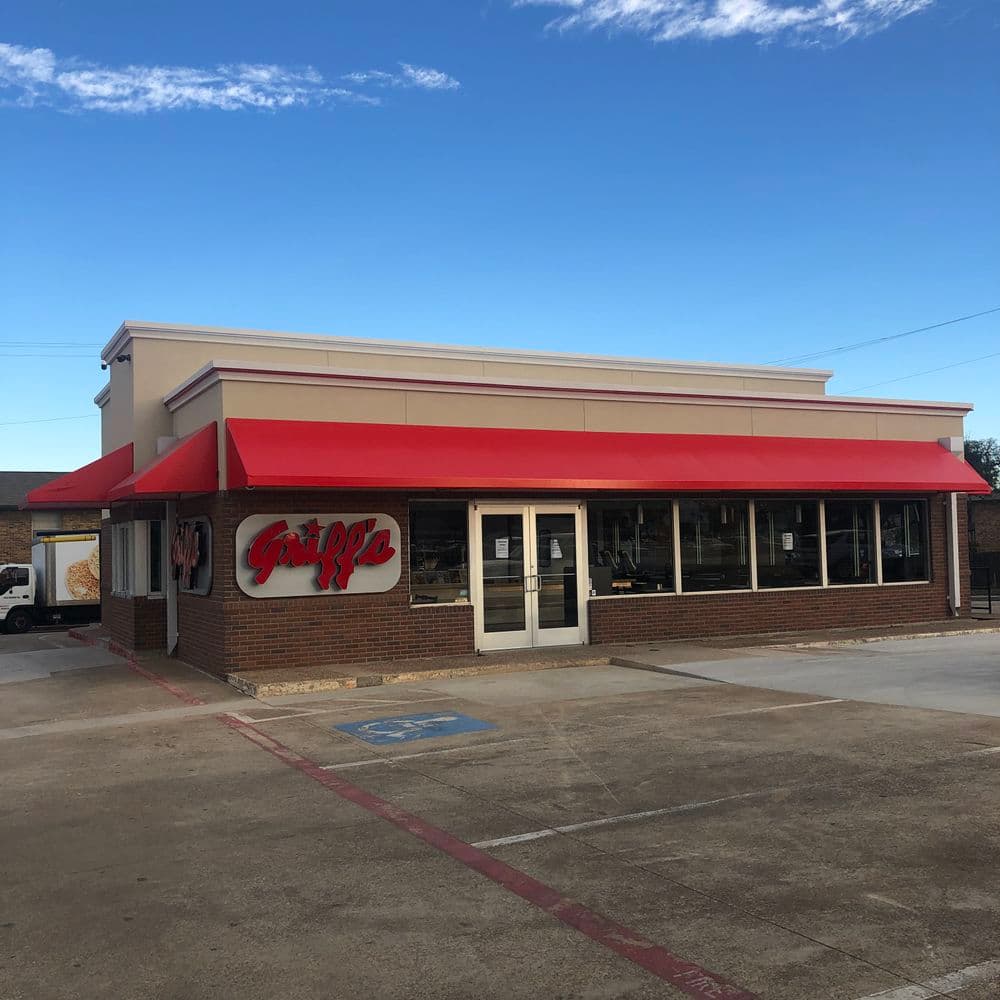 Exterior view of a restaurant with a red awning and large windows against a blue sky.