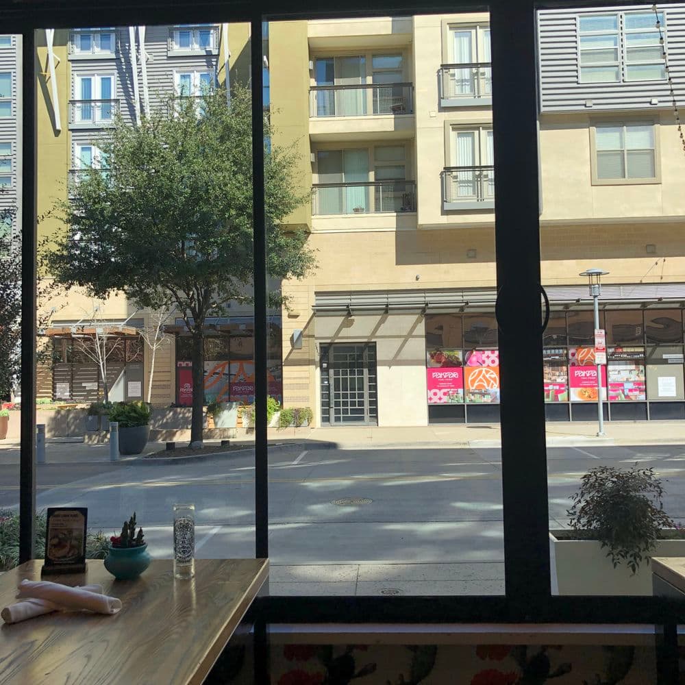 View from a cafe window showcasing modern buildings and outdoor seating area.