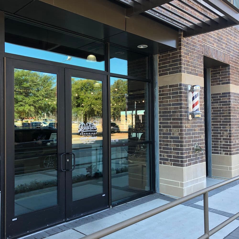 Barber shop entrance with large glass doors and brick facade, located in Dallas.