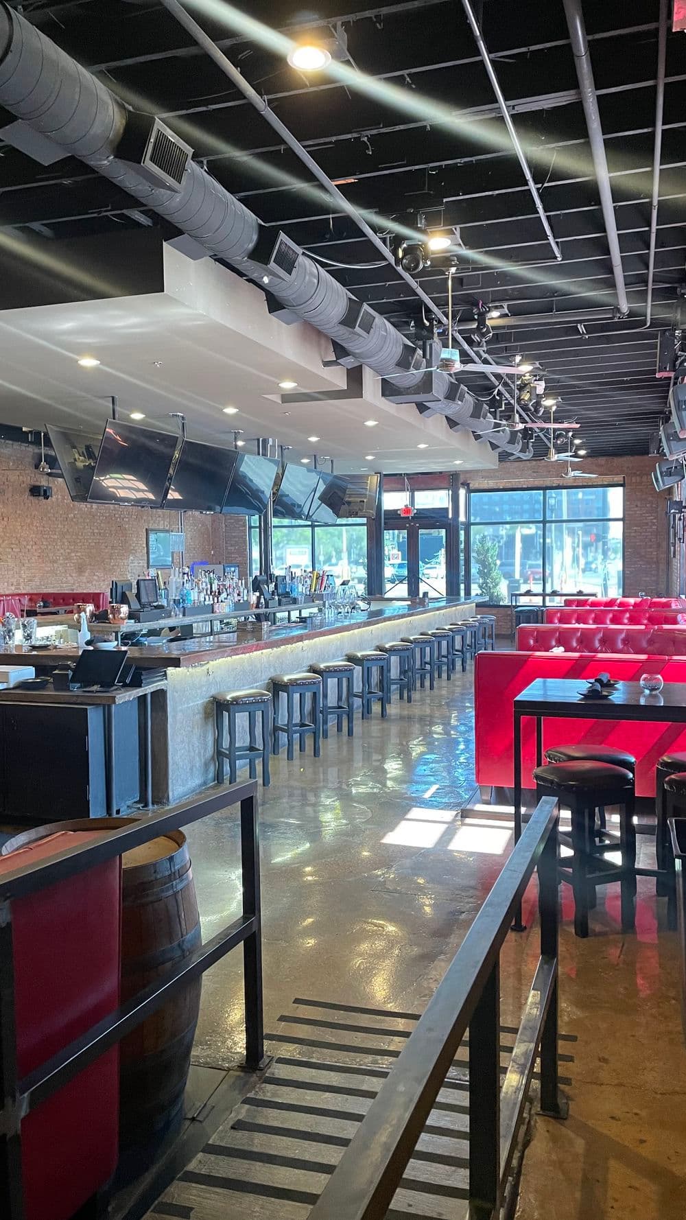 Modern bar interior with red seating, expansive bar counter, and multiple TVs displaying sports.