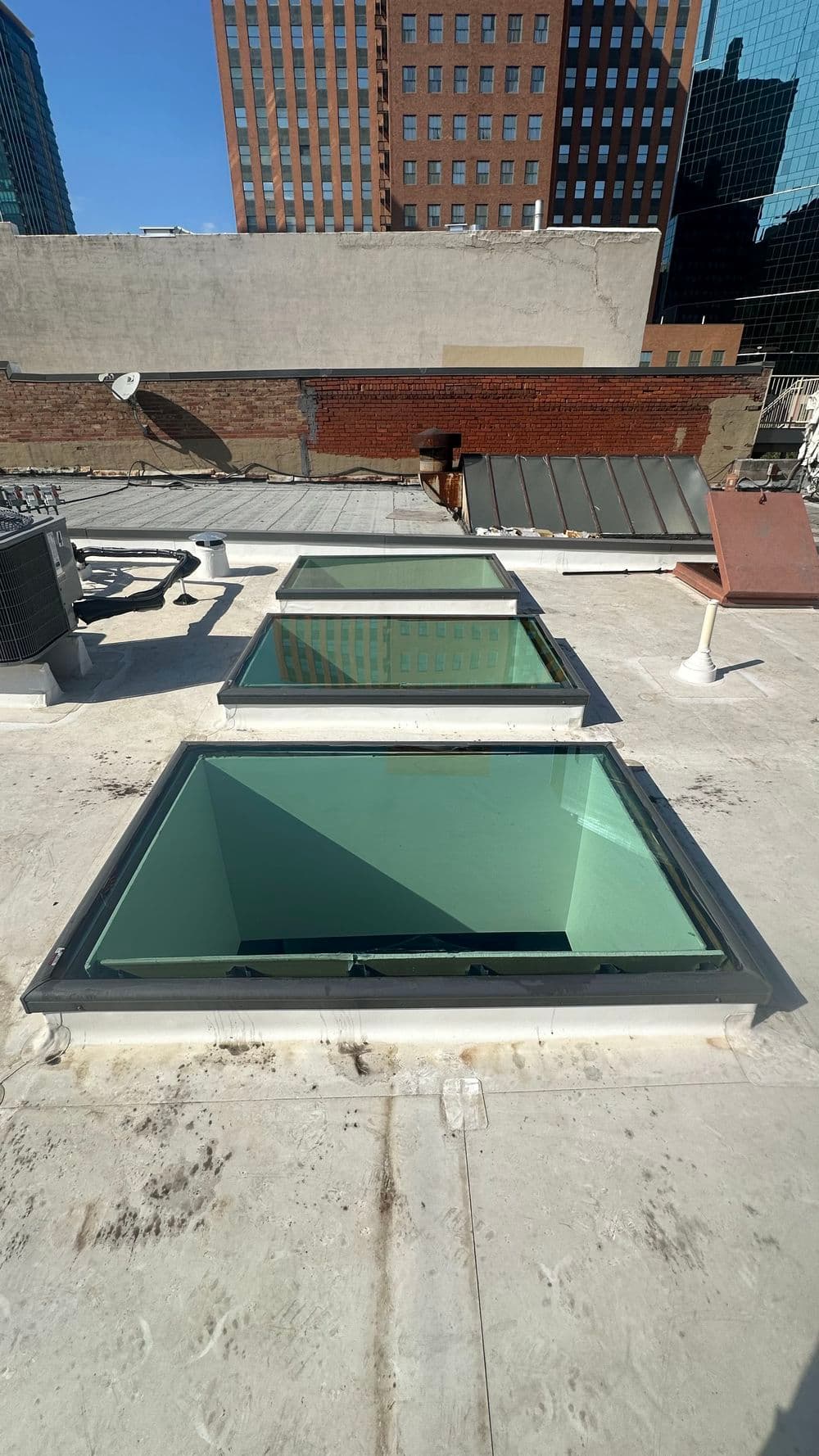Three modern skylights on a rooftop with city buildings in the background.