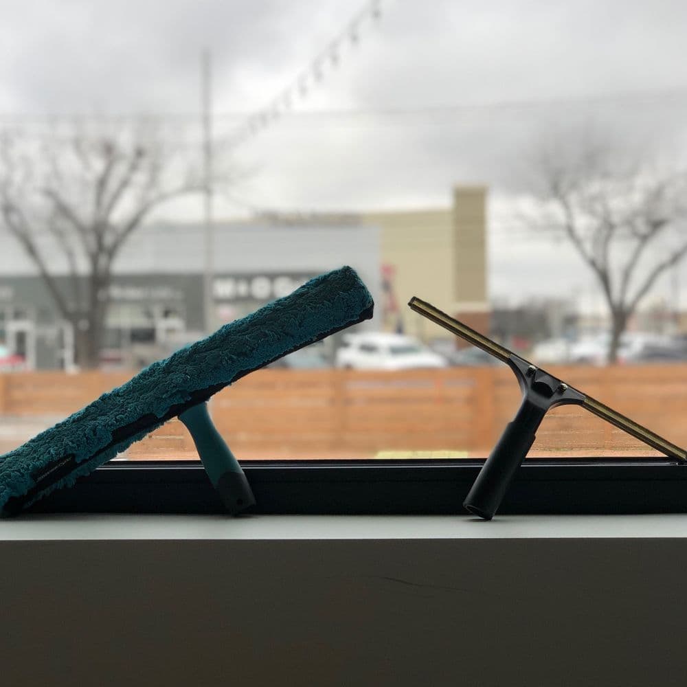 Window cleaning tools on a windowsill, with a blurred cityscape in the background.