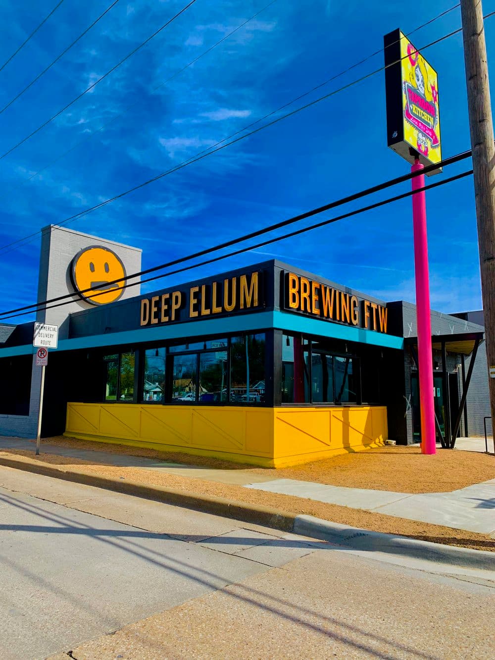 Deep Ellum Brewing exterior with vibrant yellow and black signage, sunny blue sky backdrop.