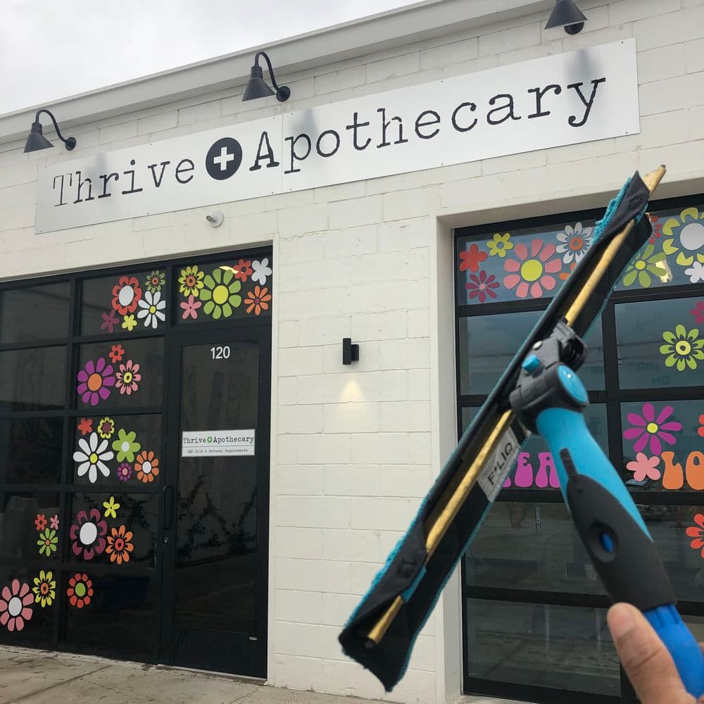 Exterior of Thrive Apothecary with colorful flower decorations and a window cleaning tool.