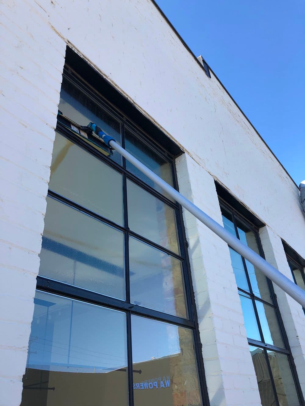 Window cleaning with a long pole on a bright day, showcasing commercial building exterior.