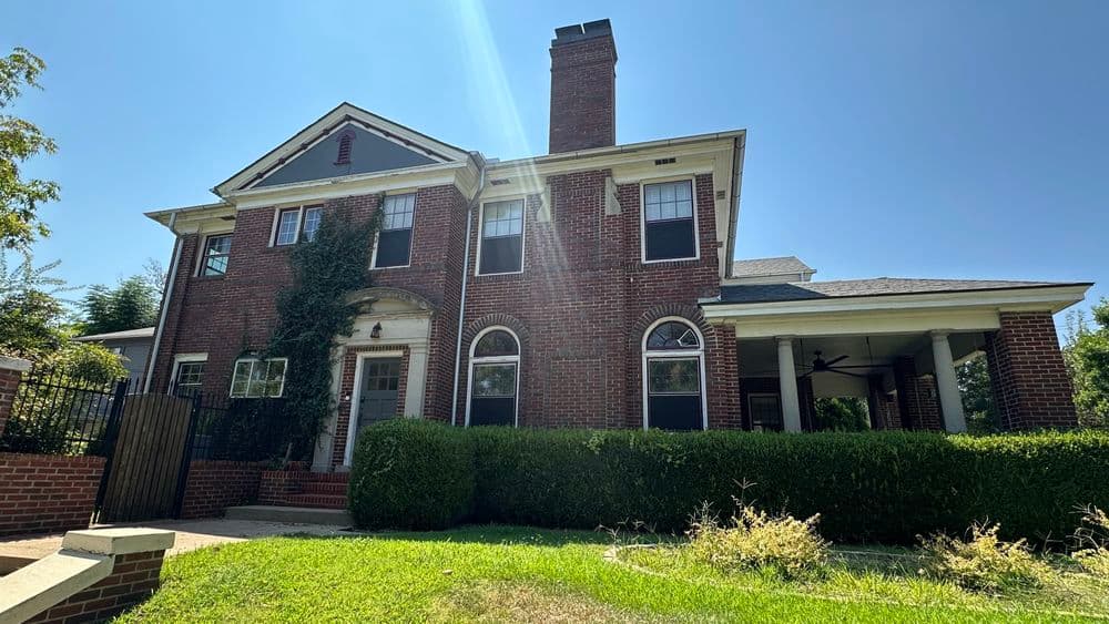 brick house with large windows and a chimney, surrounded by green grass and shrubs