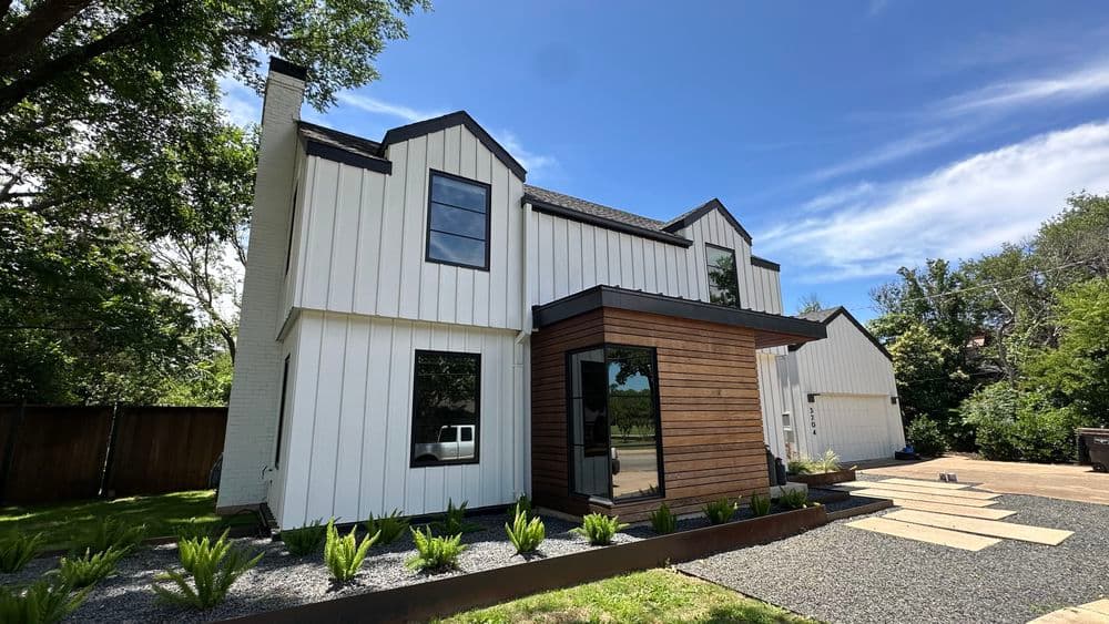 Modern two-story house with white and wood siding, large windows, and landscaped yard.