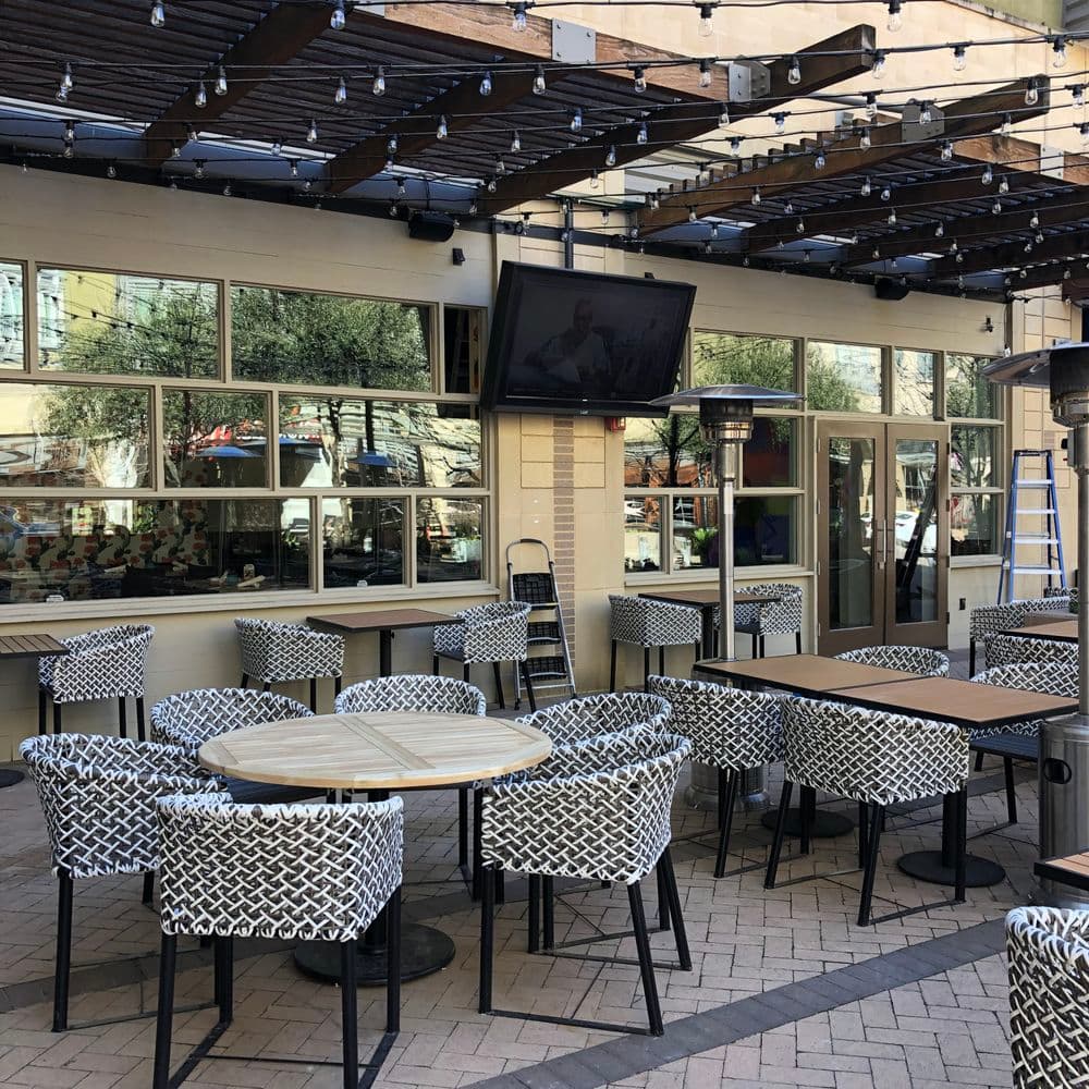 Outdoor dining area with modern chairs, wooden pergola, and a large TV screen.