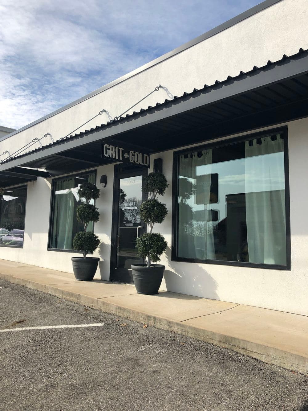 Stylish storefront of Grit + Gold with modern planters and large windows on a sunny day.