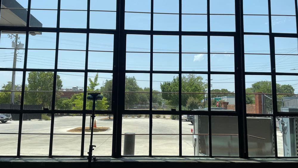 View through large industrial windows showcasing trees and an outdoor parking area.