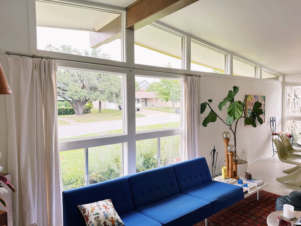 Modern living room with large windows, blue sofa, and greenery outside for a bright, airy feel.