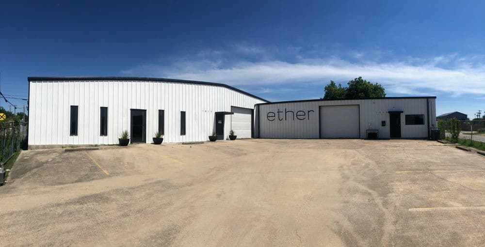 Modern white industrial building with "ether" signage and clear blue sky backdrop.