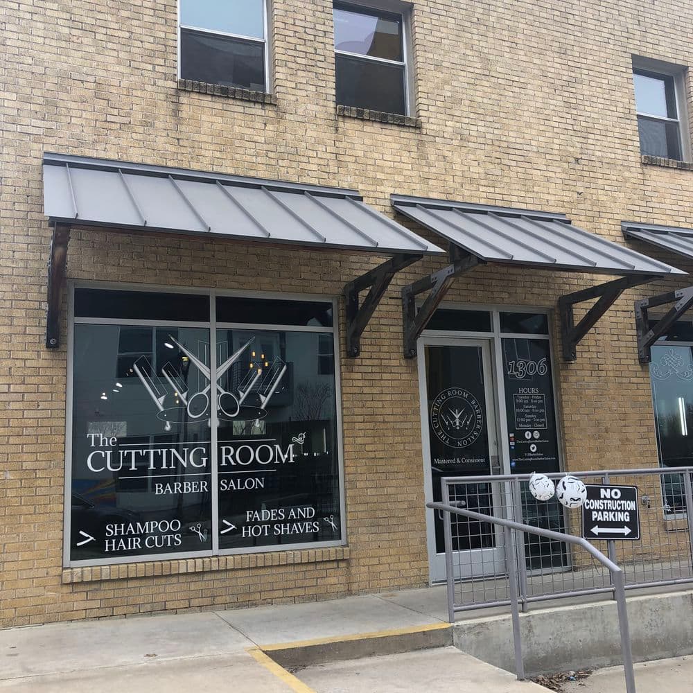 Barber salon exterior with sign for The Cutting Room, featuring haircuts and hot shaves.