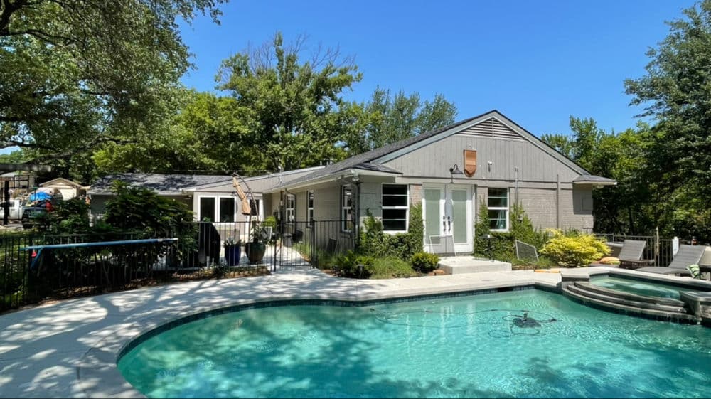Modern home with pool surrounded by lush greenery and clear blue skies. Ideal outdoor retreat.