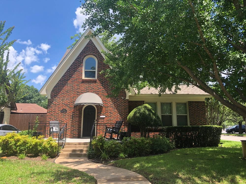 Brick home with a well-manicured lawn and lush trees under a blue sky.