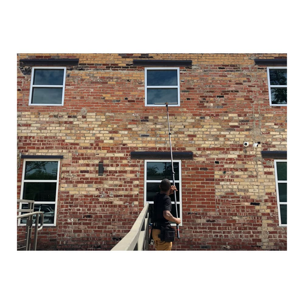 Person using a pole to clean windows on a brick building exterior.