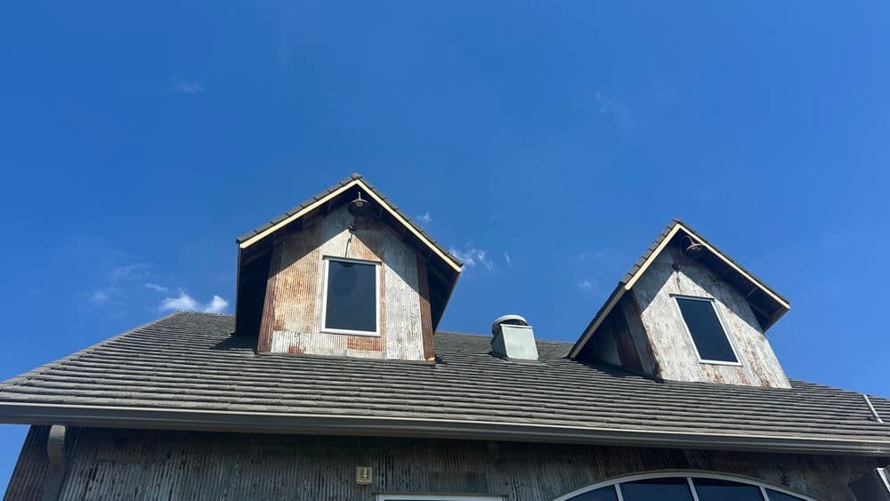 Rustic house with weathered wood siding and two gabled windows against a clear blue sky.