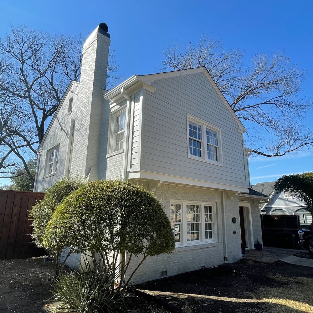 Charming white house with landscaped shrubs and a clear blue sky. Ideal suburban home exterior.
