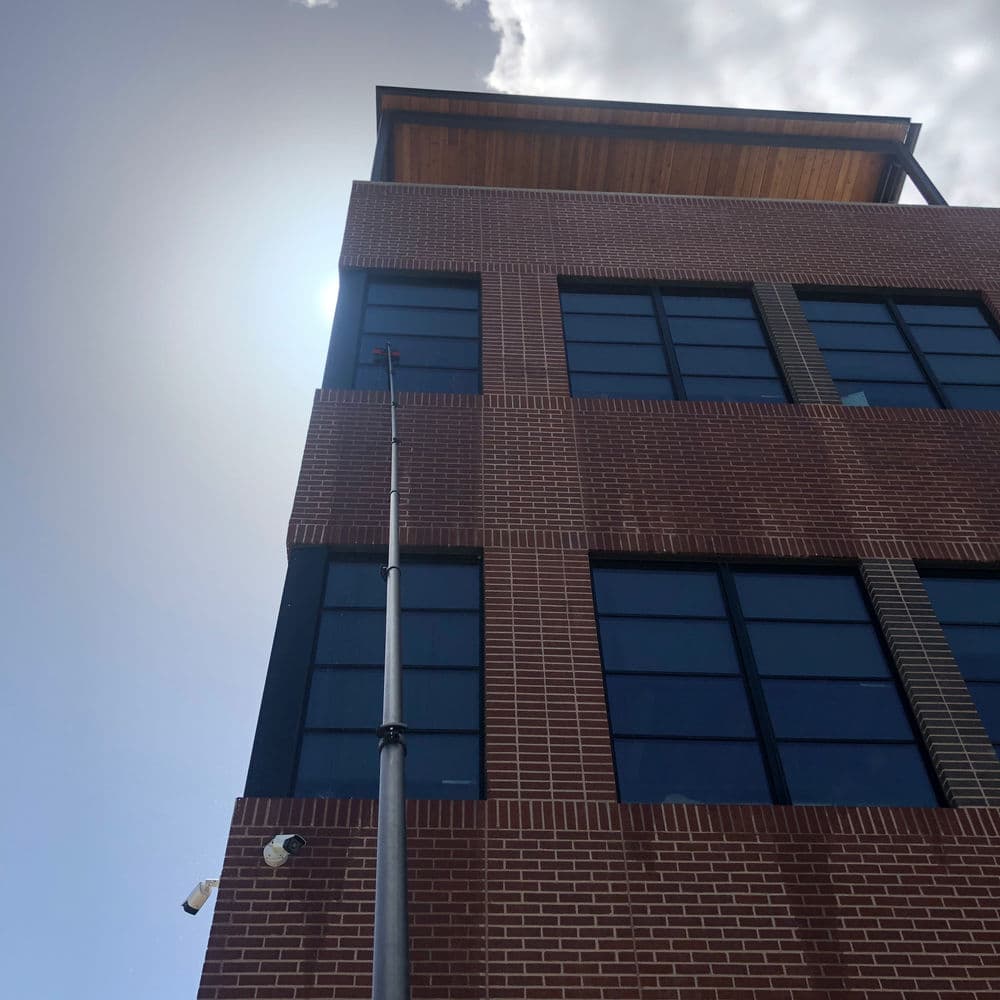 View of a modern brick building under a clear sky with sun glare and surveillance cameras.